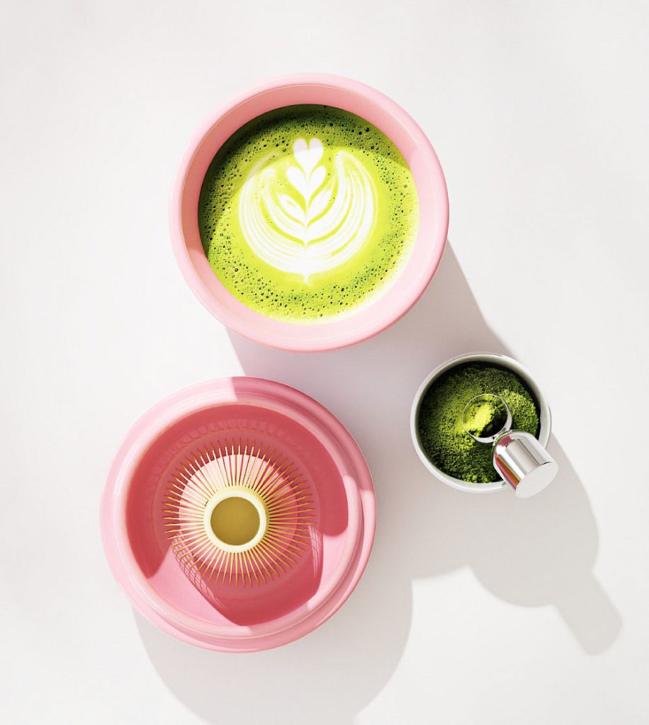 Pink ceramic matcha bowl filled with bright green matcha latte, shown with whisk holder and scoop.
