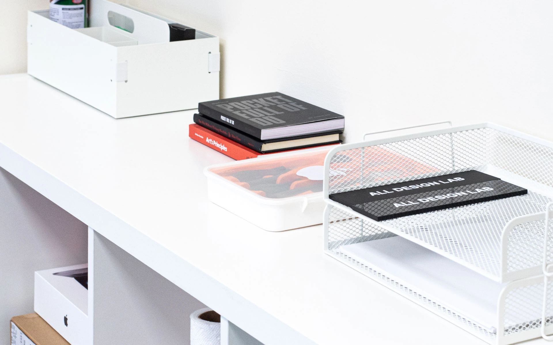 Minimal office shelf with All Design Lab notebooks, design books, and organized stationery in white containers.