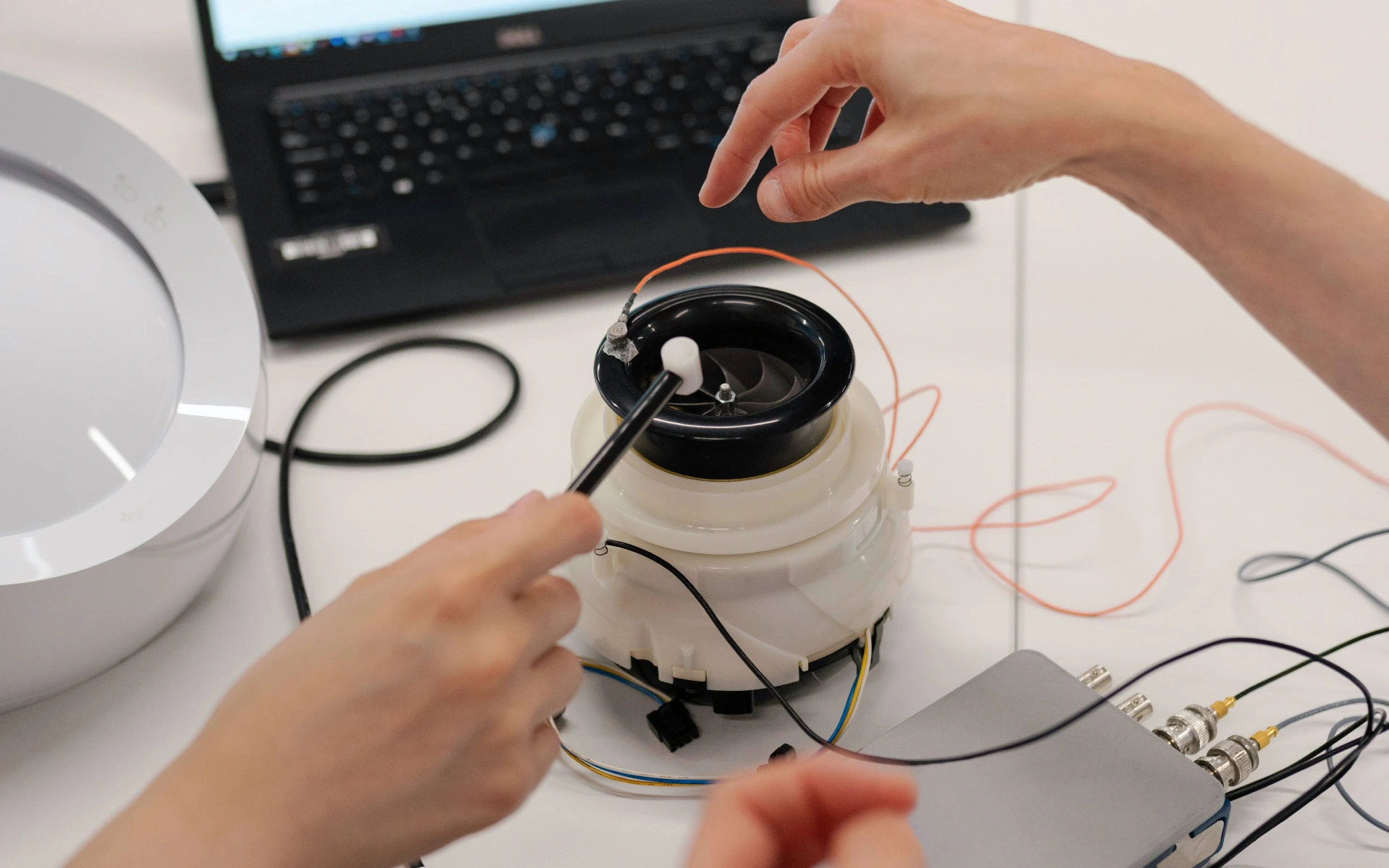 Engineers testing a prototype device with sensors and wiring connected to a laptop during product development.