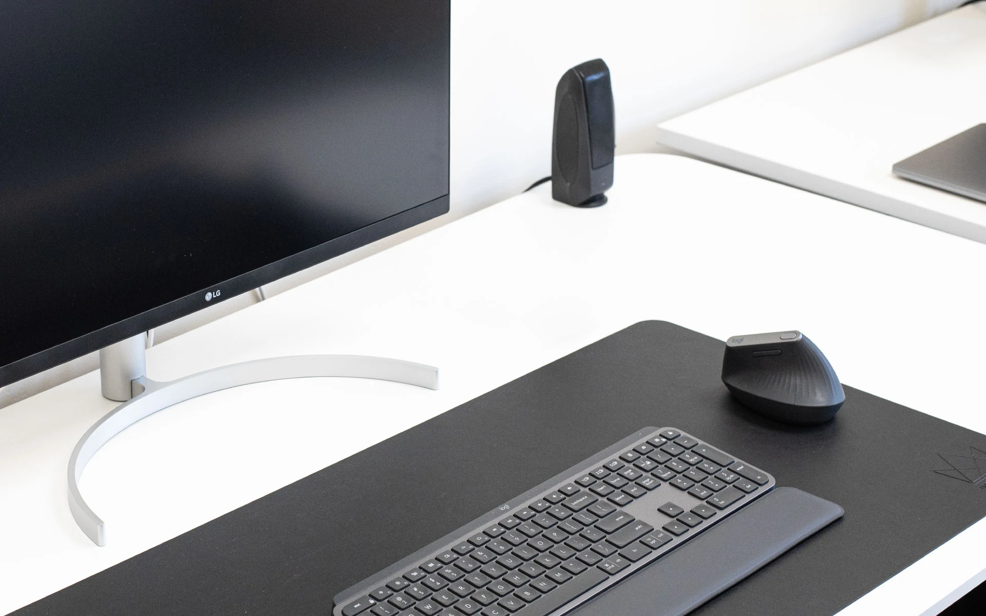 Clean modern workspace with a large monitor, keyboard, and ergonomic mouse on a black desk mat.