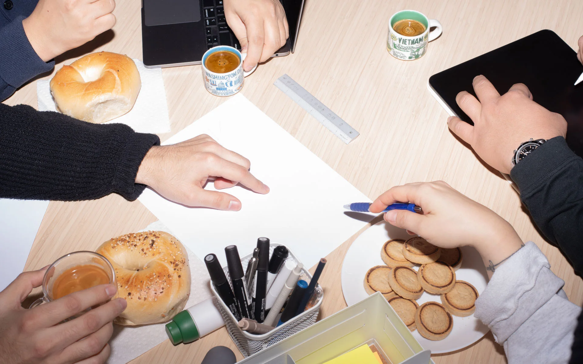 esign team collaborating over sketches and laptops on a table with coffee, bagels, and cookies during a brainstorming session.