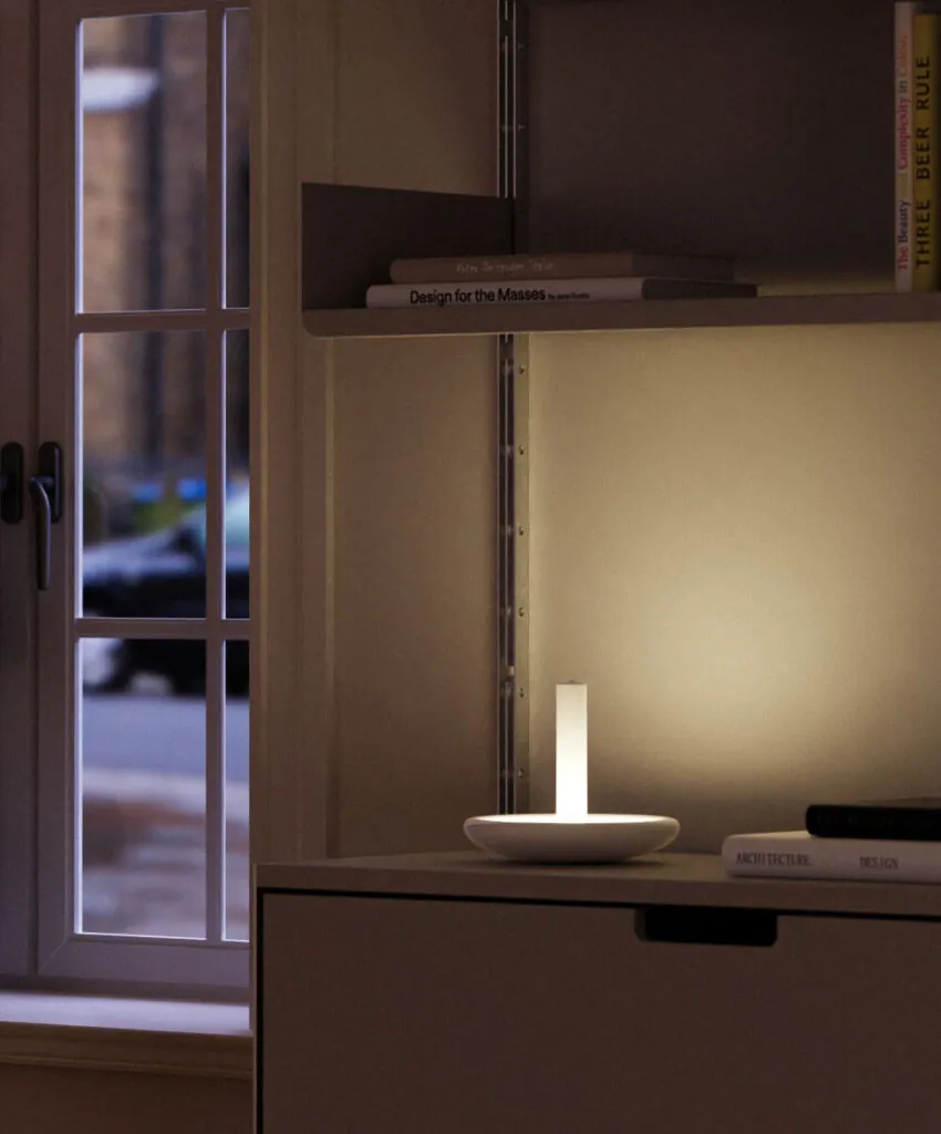 Cabinet, and books and white wall illuminated by lamp. Beacon Portable Table Lamp by All Design Lab.