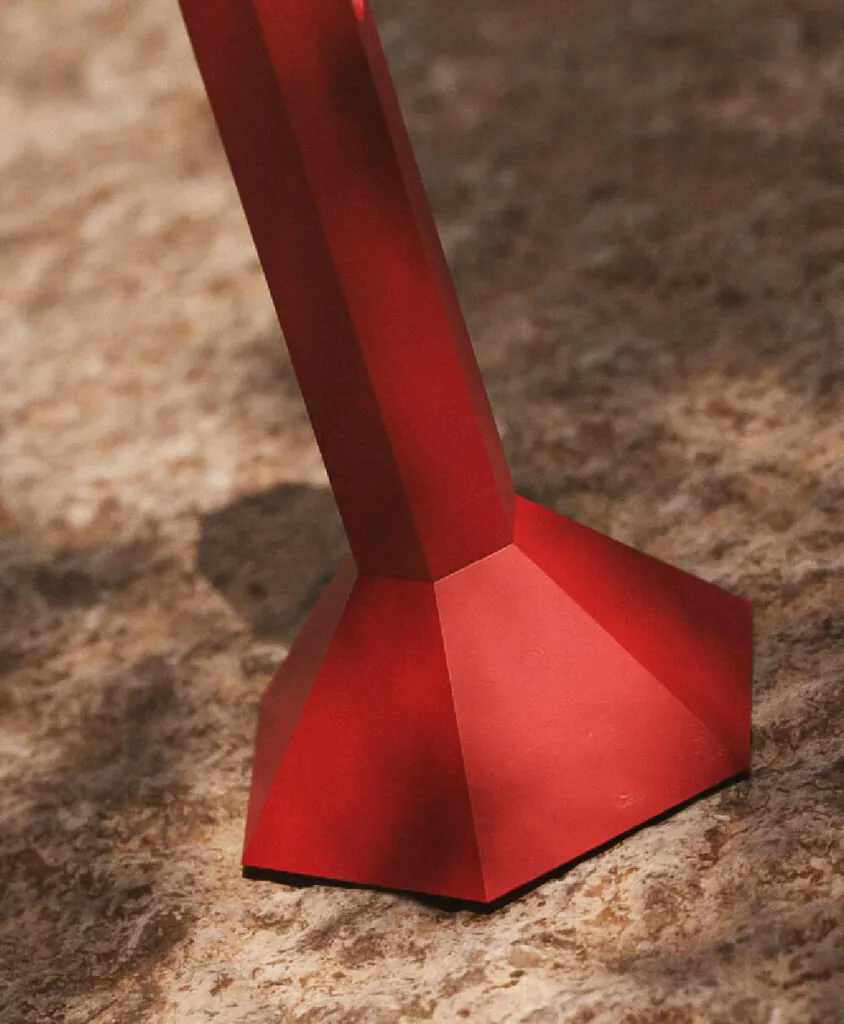 A hexagonal shaped red metal flashlight resting on top of a rock. Hex tools flashlight by All Design Lab.