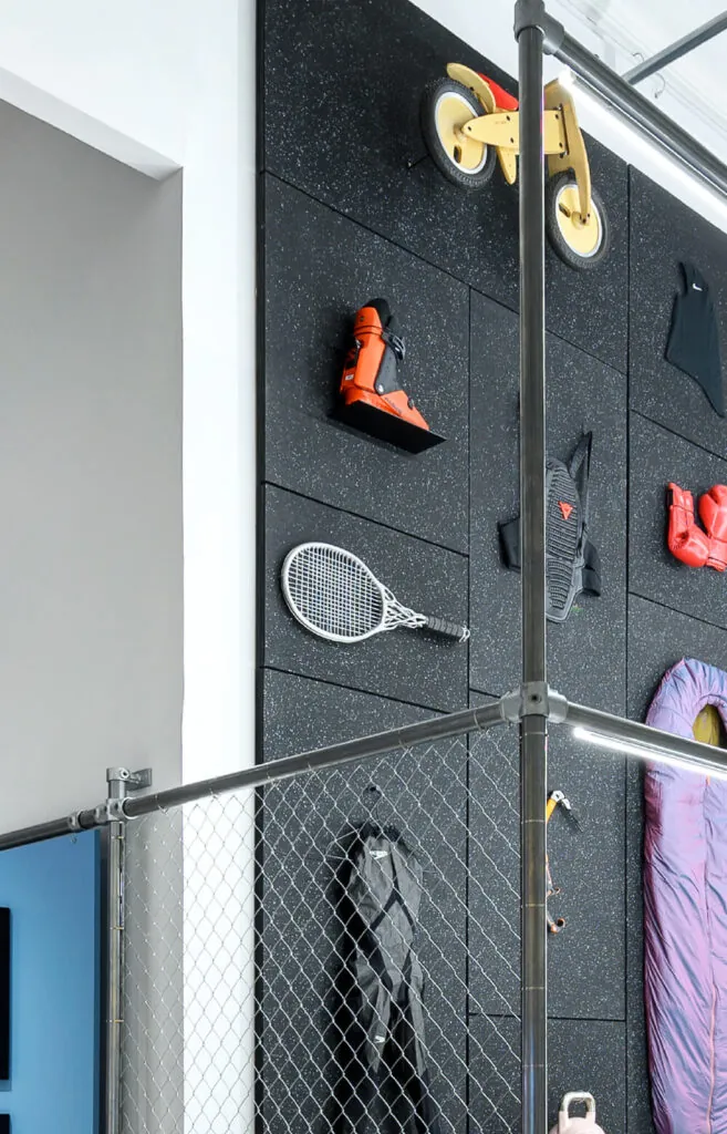 Black wall of products, metal tennis racket, snow boots, wooden bike. Hìtëkw Tennis Racket by All Design Lab.