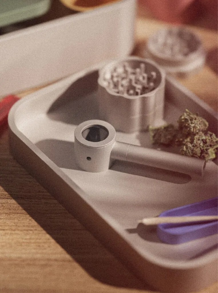 A pipe lies on a tray with a grinder and herb, suggesting preparation for use. Mango Storage System by All Design Lab.