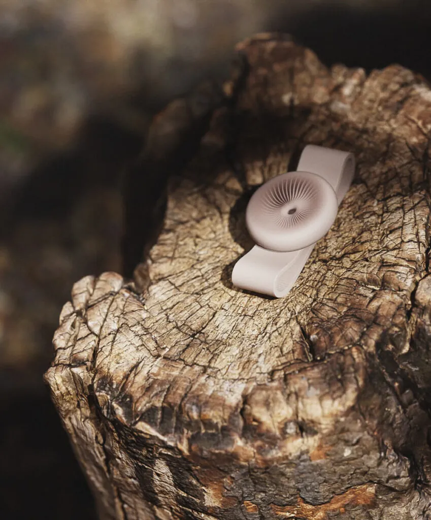 A beige wristband with a detailed disk on a textured tree stump. Momentum Smartwatch by All Design Lab.