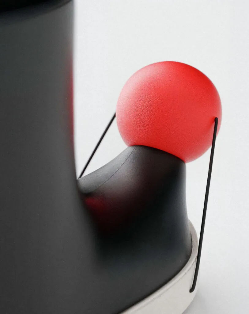 Close up of red ball on toe of black boots connected by a string. Pom footwear by All Design Lab.