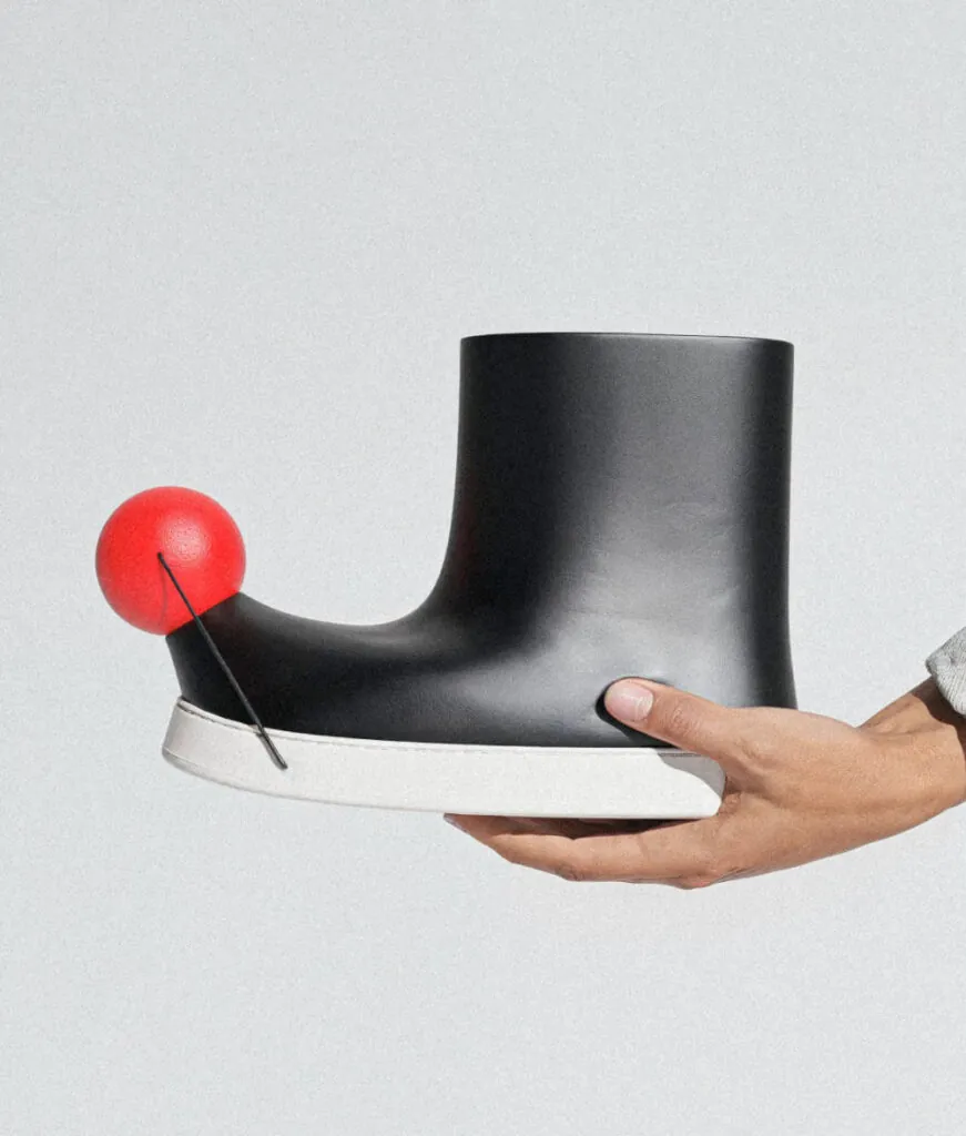Hand holding black minimal boots with red ball on toe. Pom footwear by All Design Lab.