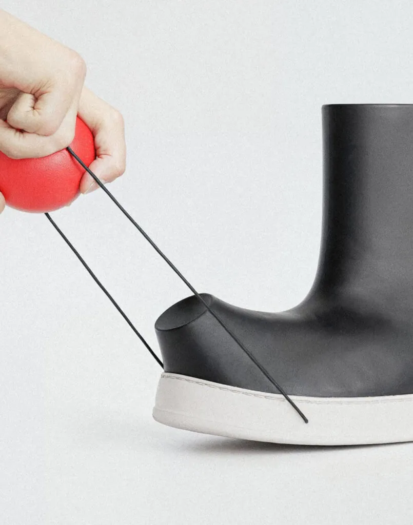 Hand holding red ball contected to black boots. Pom footwear by All Design Lab.