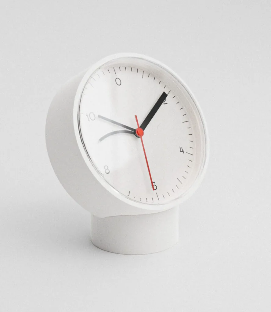 White table clock on white background, red second hand. Tardi Table Clock by All Design Lab.