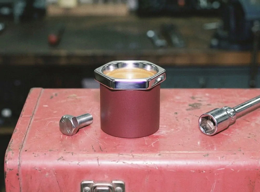 Esagono espresso cup with fresh espresso on scratched red metal toolbox, single hex bolt and chrome socket wrench alongside, shot on expired 35mm film