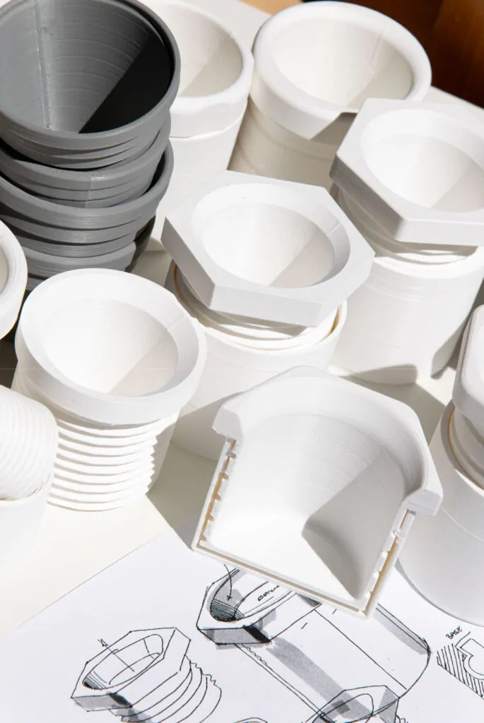 Esagono espresso cup design process — white and grey FDM 3D printed prototypes at multiple stages alongside hand sketches on paper